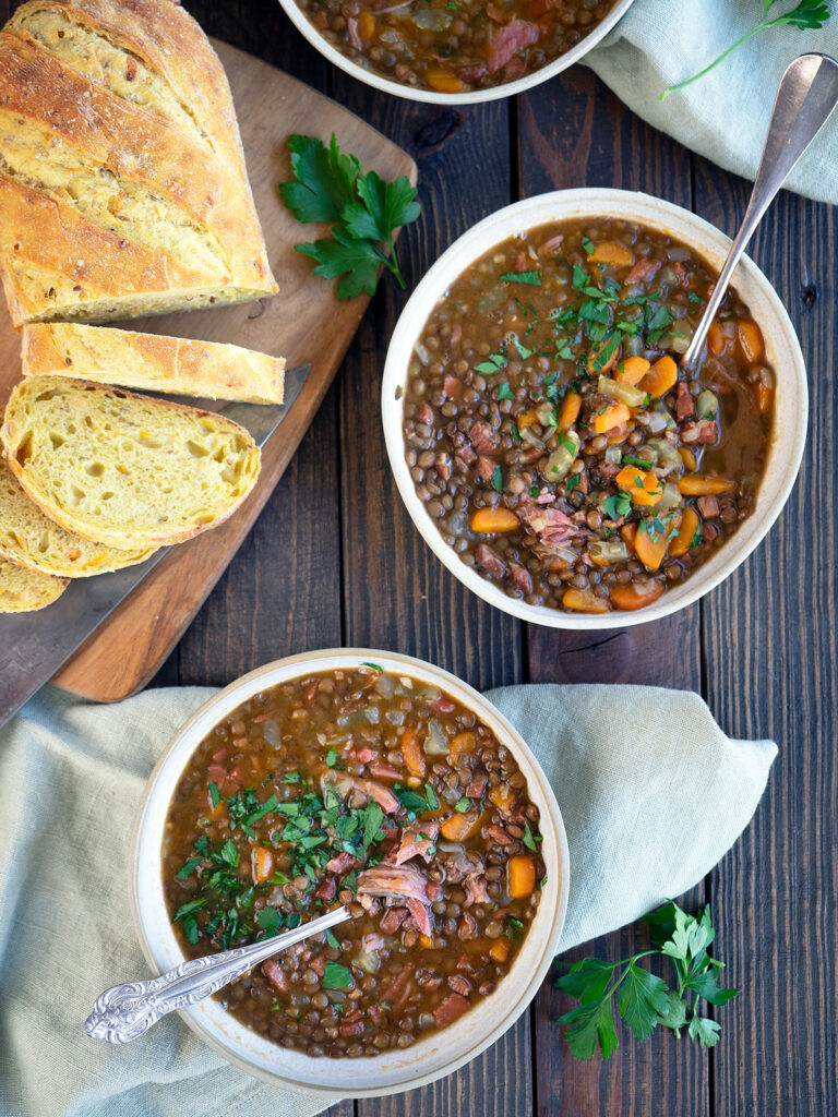 ham and lentil soup in bowls with bread on a cutting board