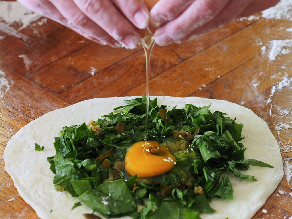 cracking an egg over spinach filling on rolled dough