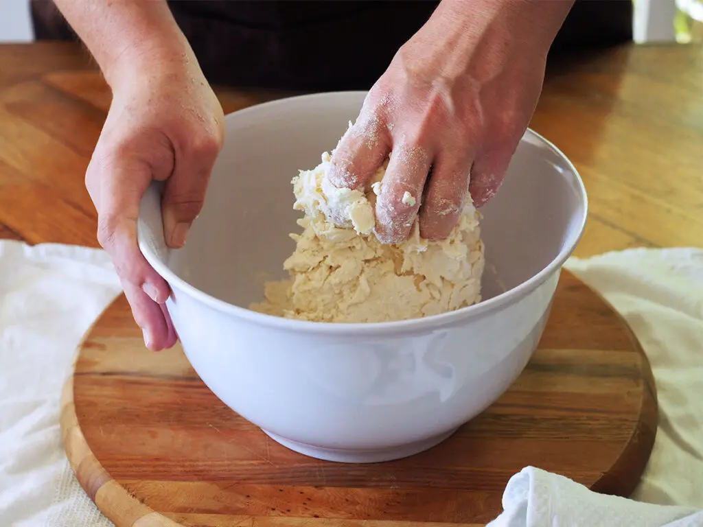 mixing dough by hand in a white plastic bowl