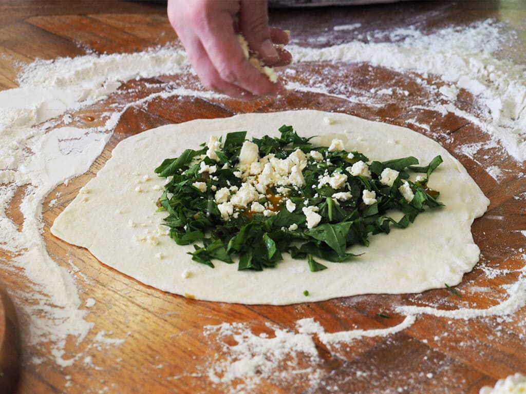 hand sprinkling crumbles feta over spinach for gozleme filling