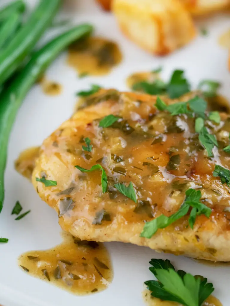 close up of chicken in lemon sauce with beans and potatoes in the back ground