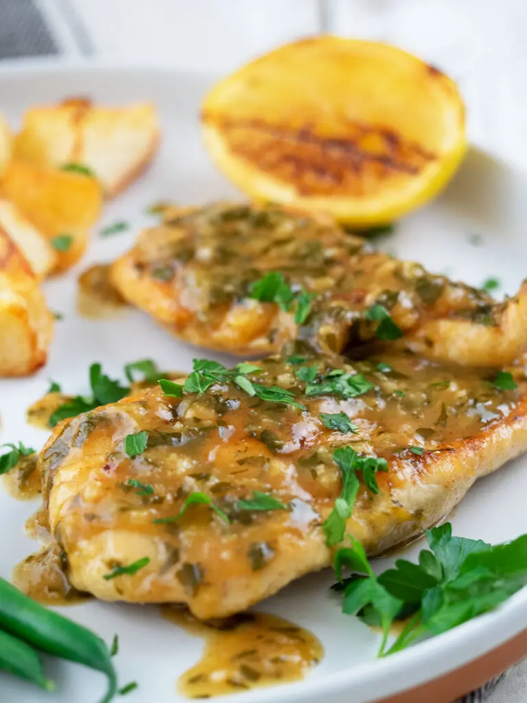 chicken in lemon sauce on a white plate with a lemon cheek