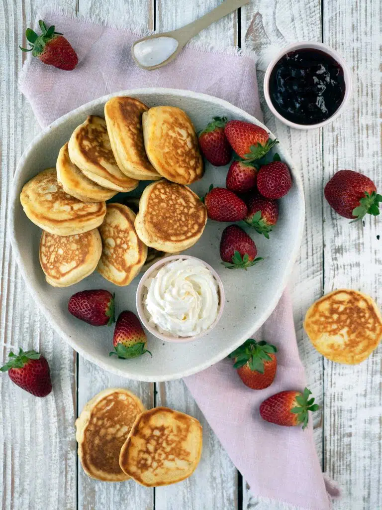 pikelets on a serving palte with strawberry jam and cream