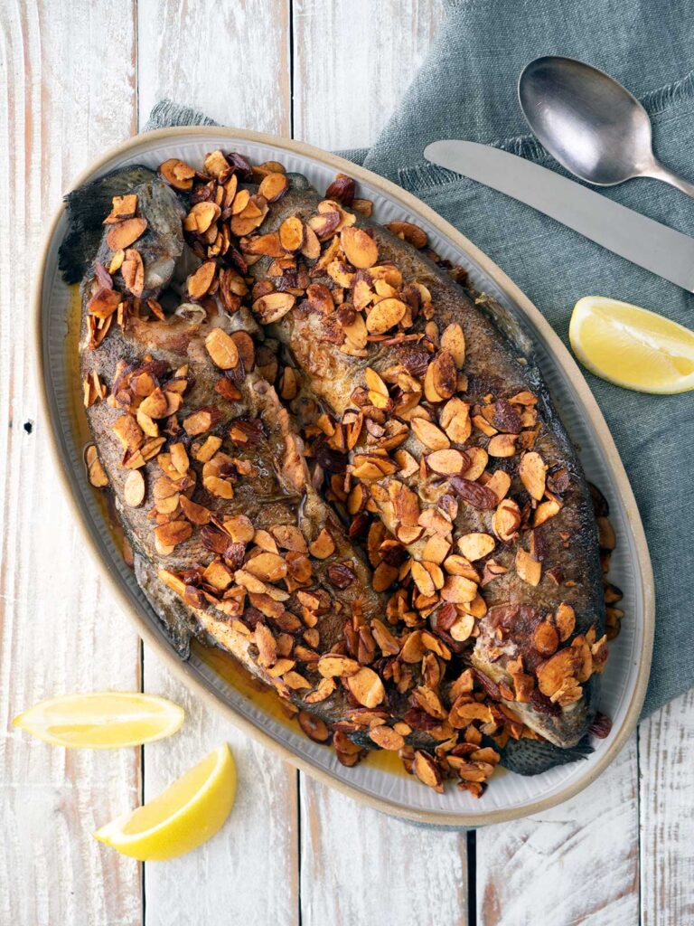 trout almondine on a serving plate with lemon wedges scattered around