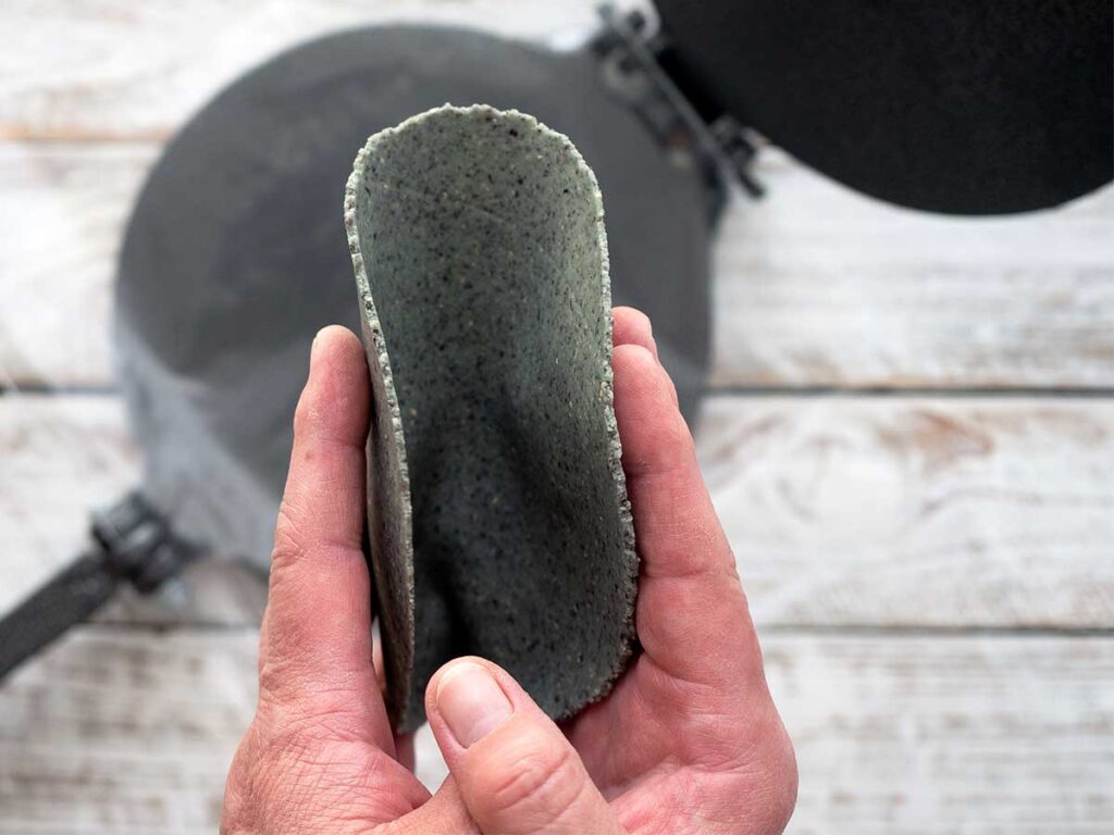 freshly pressed blue corn tortilla being held to show the thickness