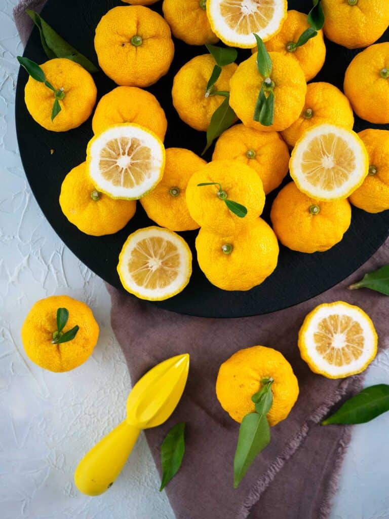 A selection of yuzu on a plate, some are whole, some are cut in half.