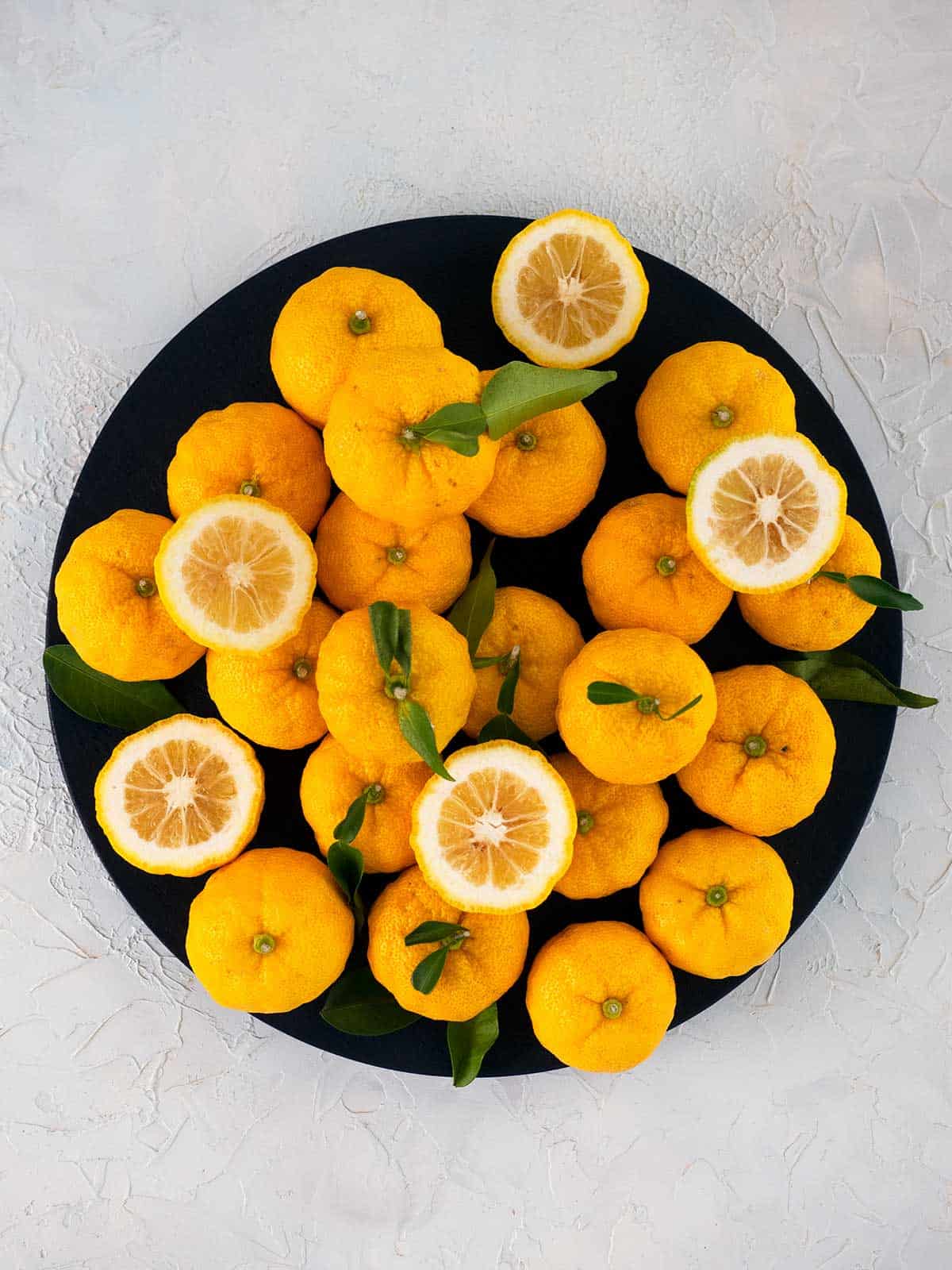 A selection of yuzu on a plate, some are whole, some are cut in half.