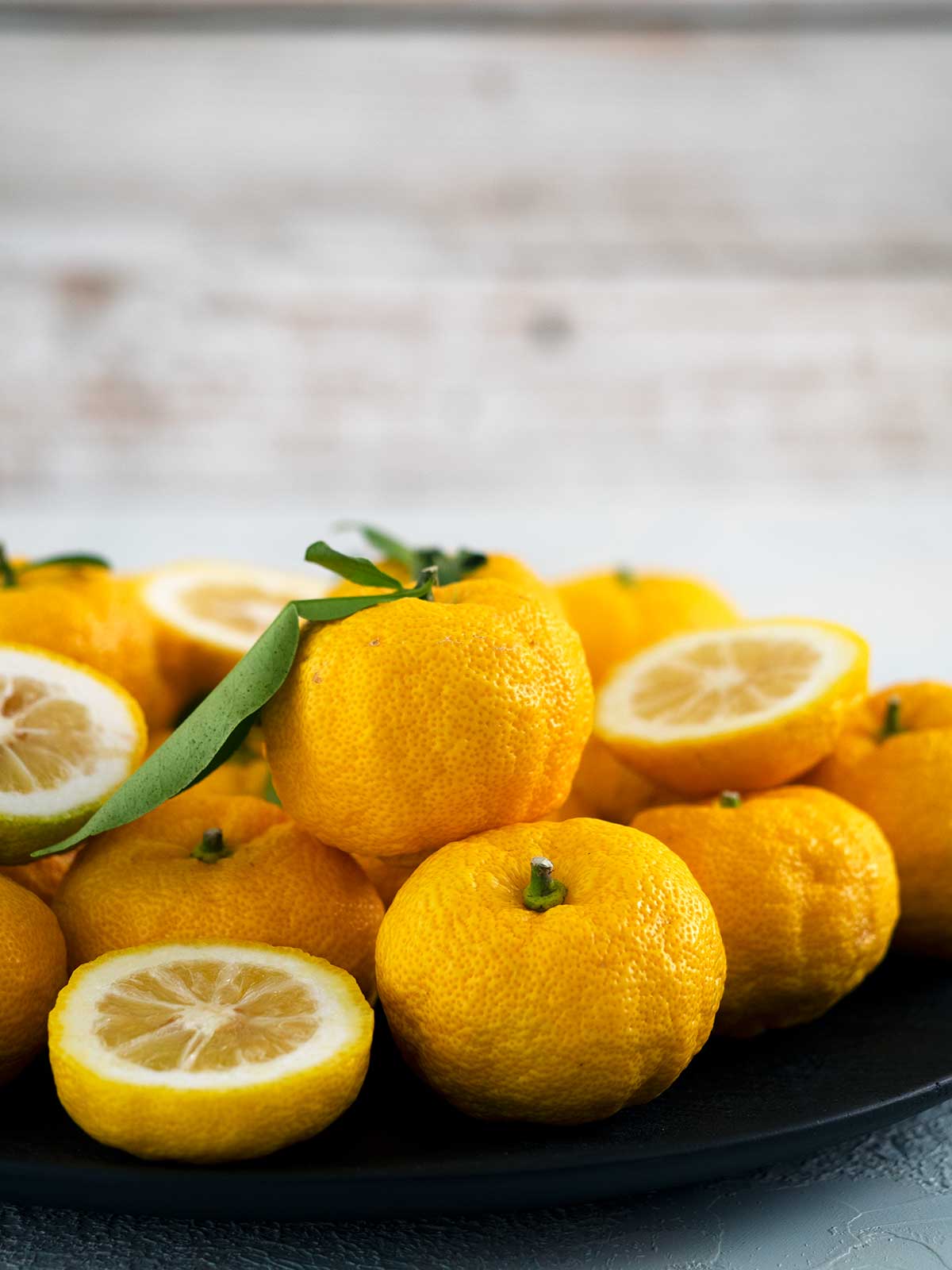 A selection of yuzu on a plate, some are whole, some are cut in half.