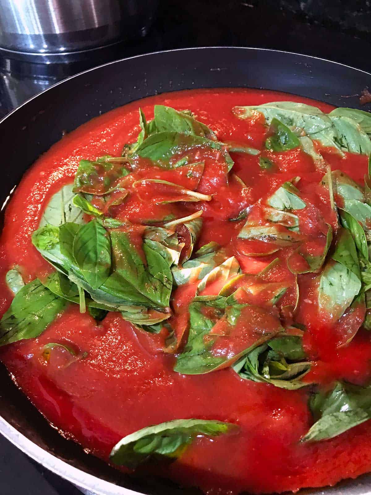 Adding basil to the tomato sauce cooking in the frying pan.