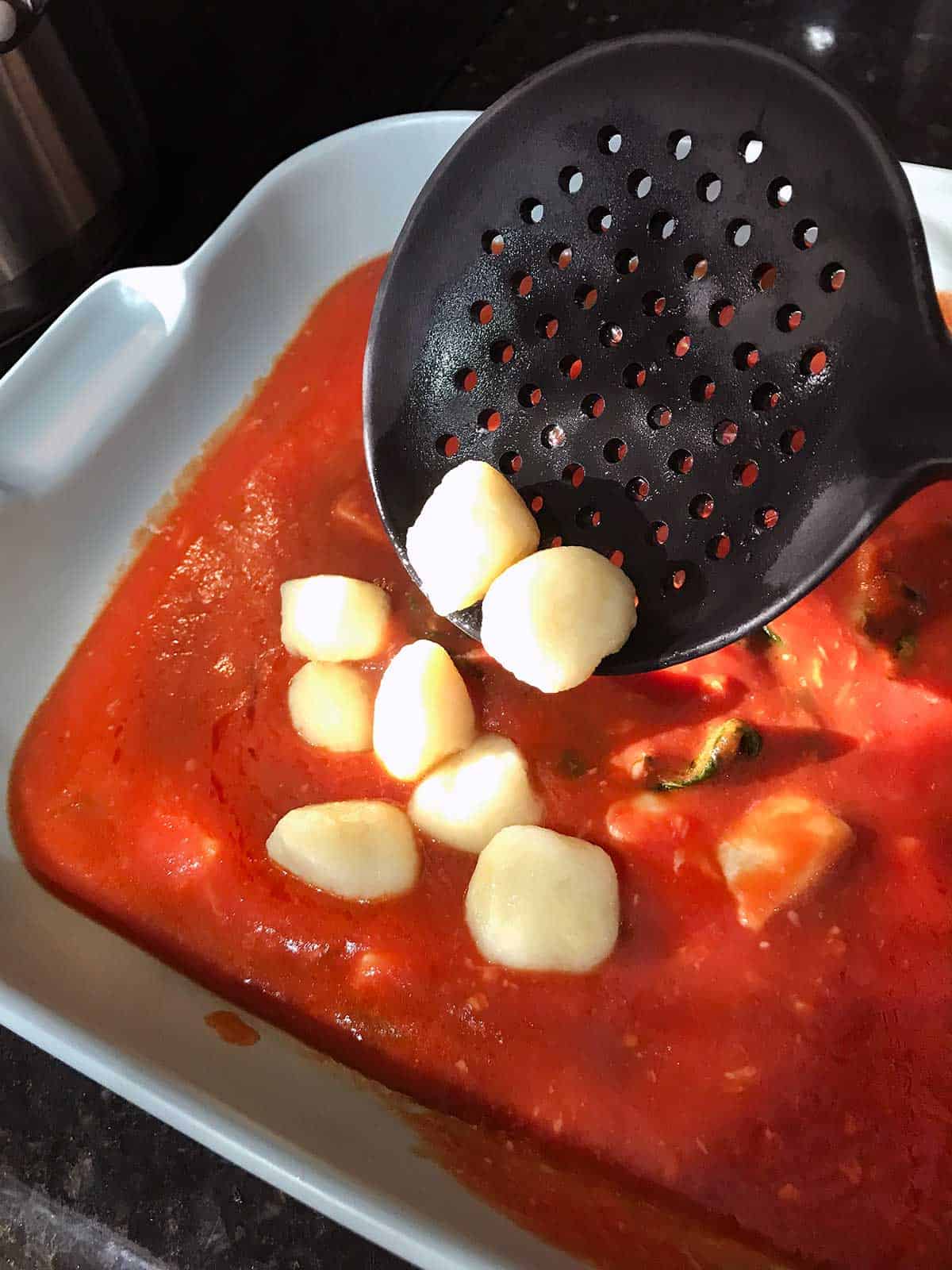 Adding cooked gnocchi to the tomato sauce in the baking dish.