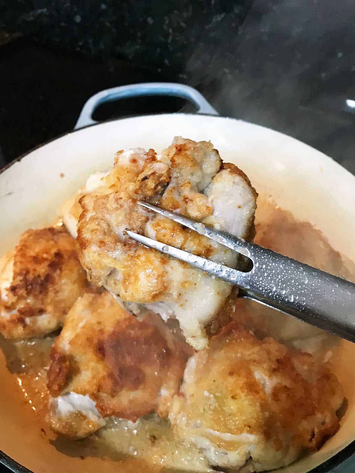 Tongs picking up and showing the underside of the browned chicken thigh.