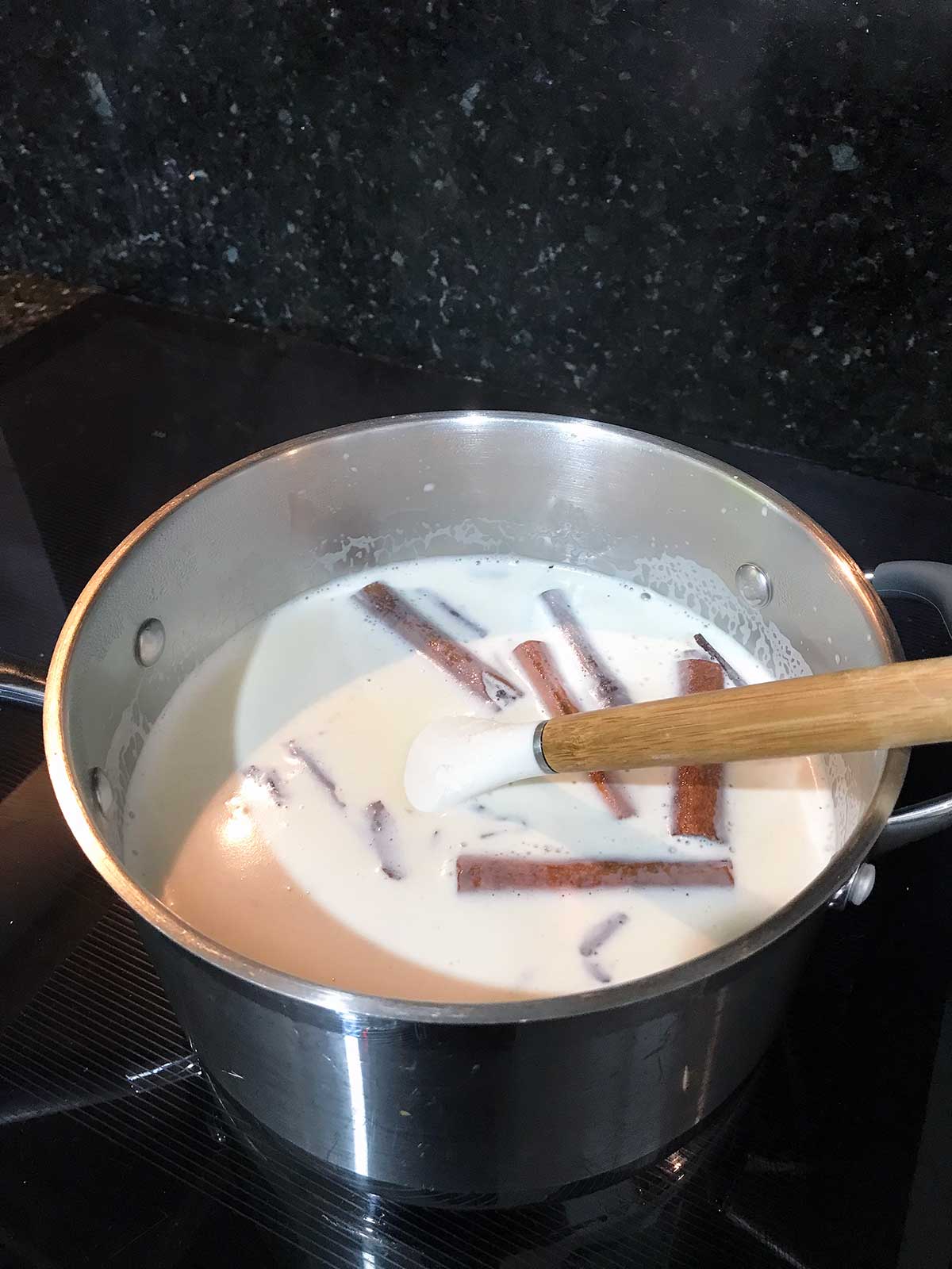 Milk, sugar, and spices in a pot on the stove.