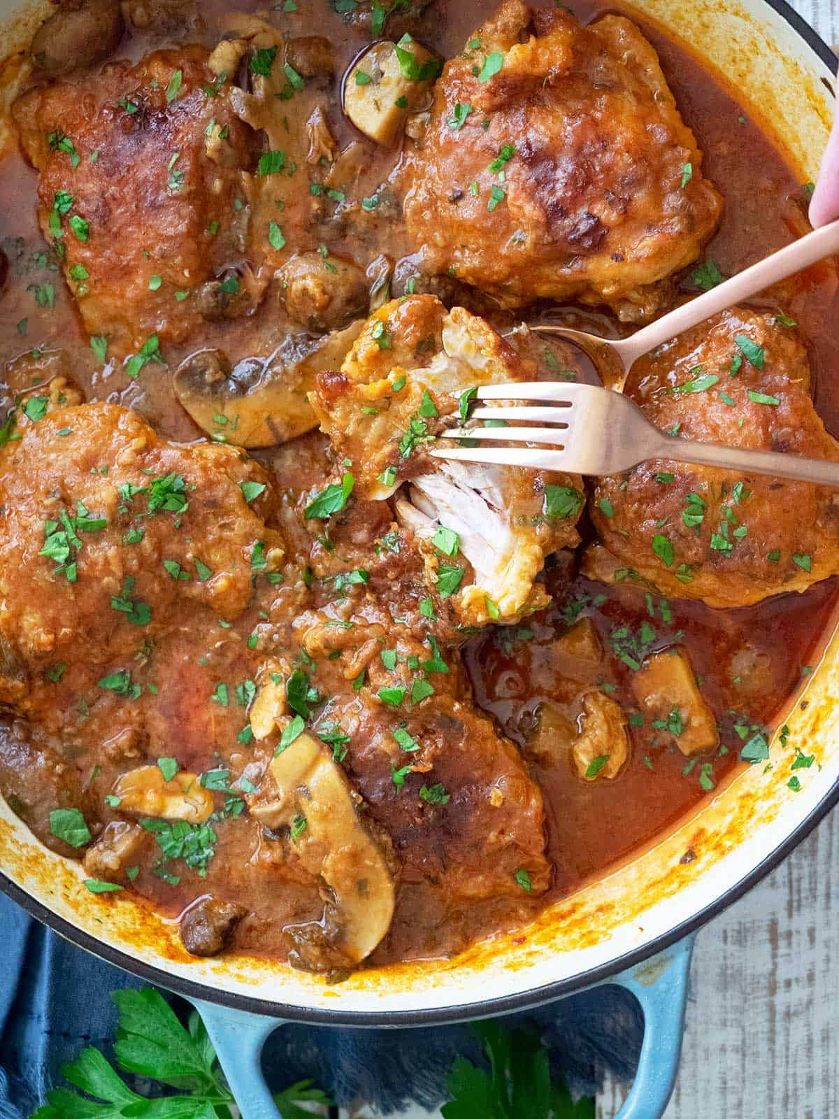 A fork and spoon breaking a piece of chicken thigh apart in the pan to show how tender it is.