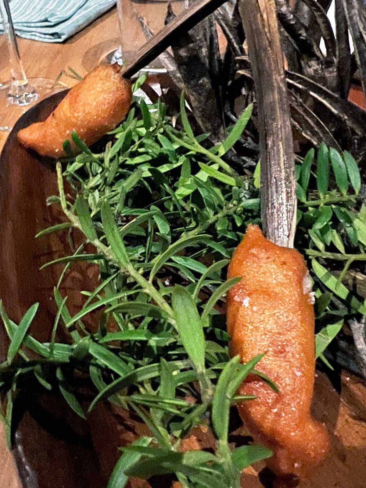 Ahi scampi corn dogs served on a stick on a bed of green leaves.