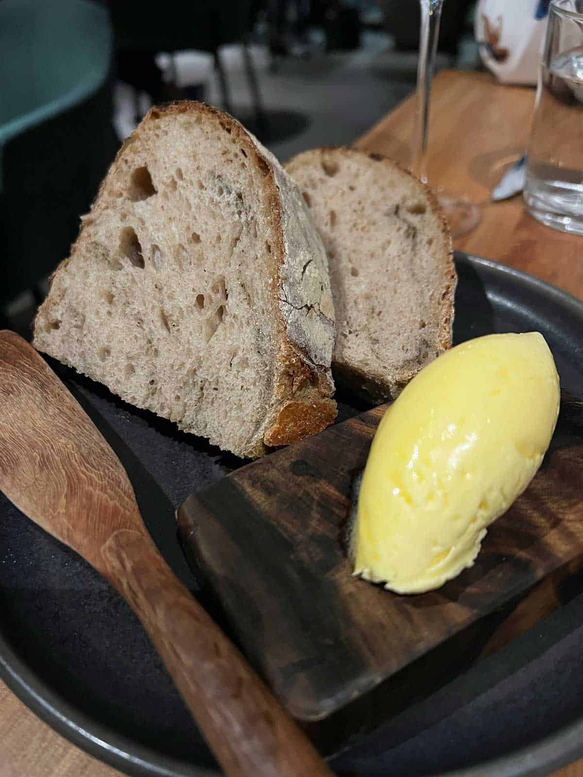 Ahi Kawakawa sourdough and butter on a plate with a wooden knife.