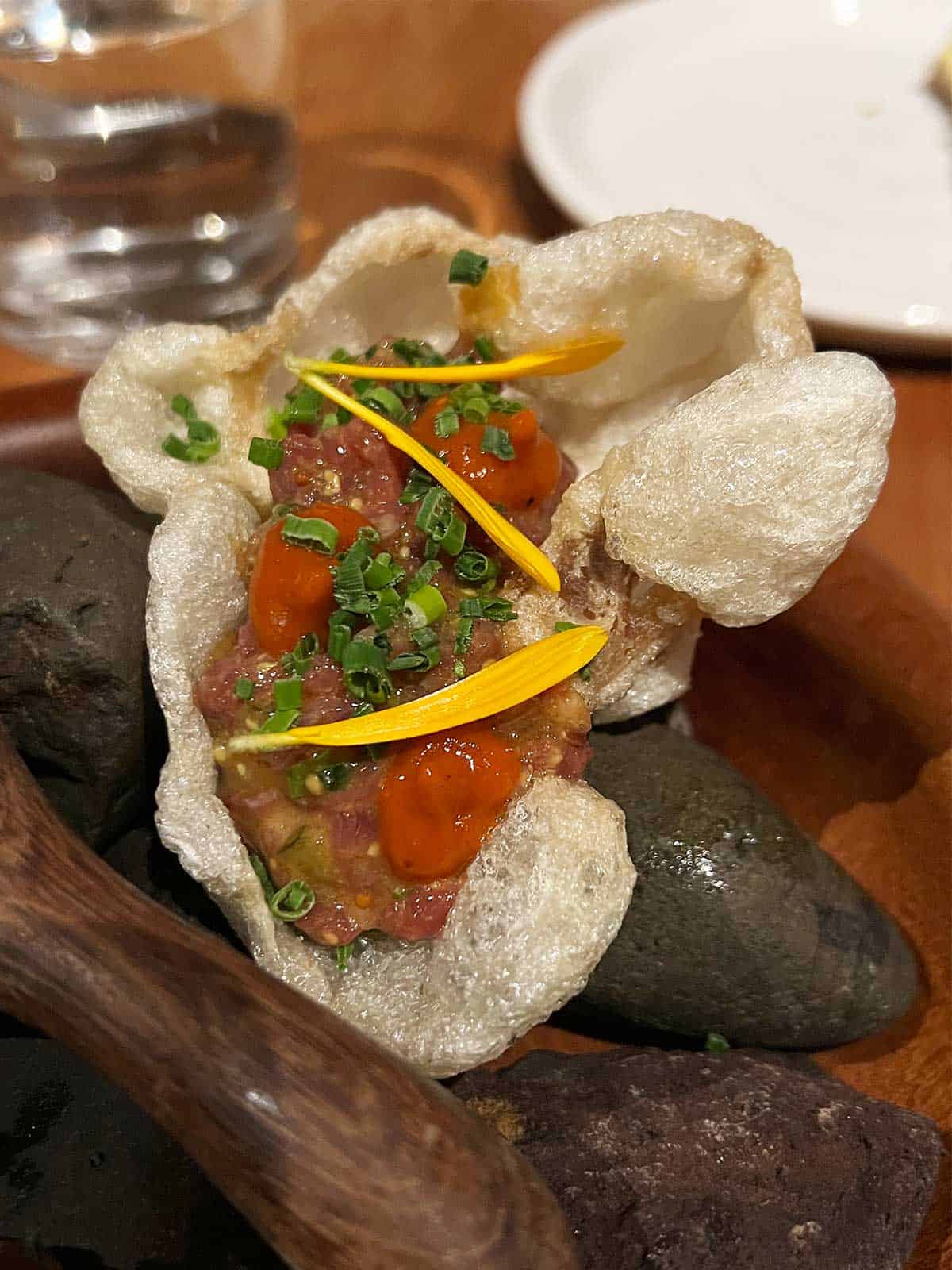 Wallaby tartare in a puffed wagyu tendon sitting on some rocks.