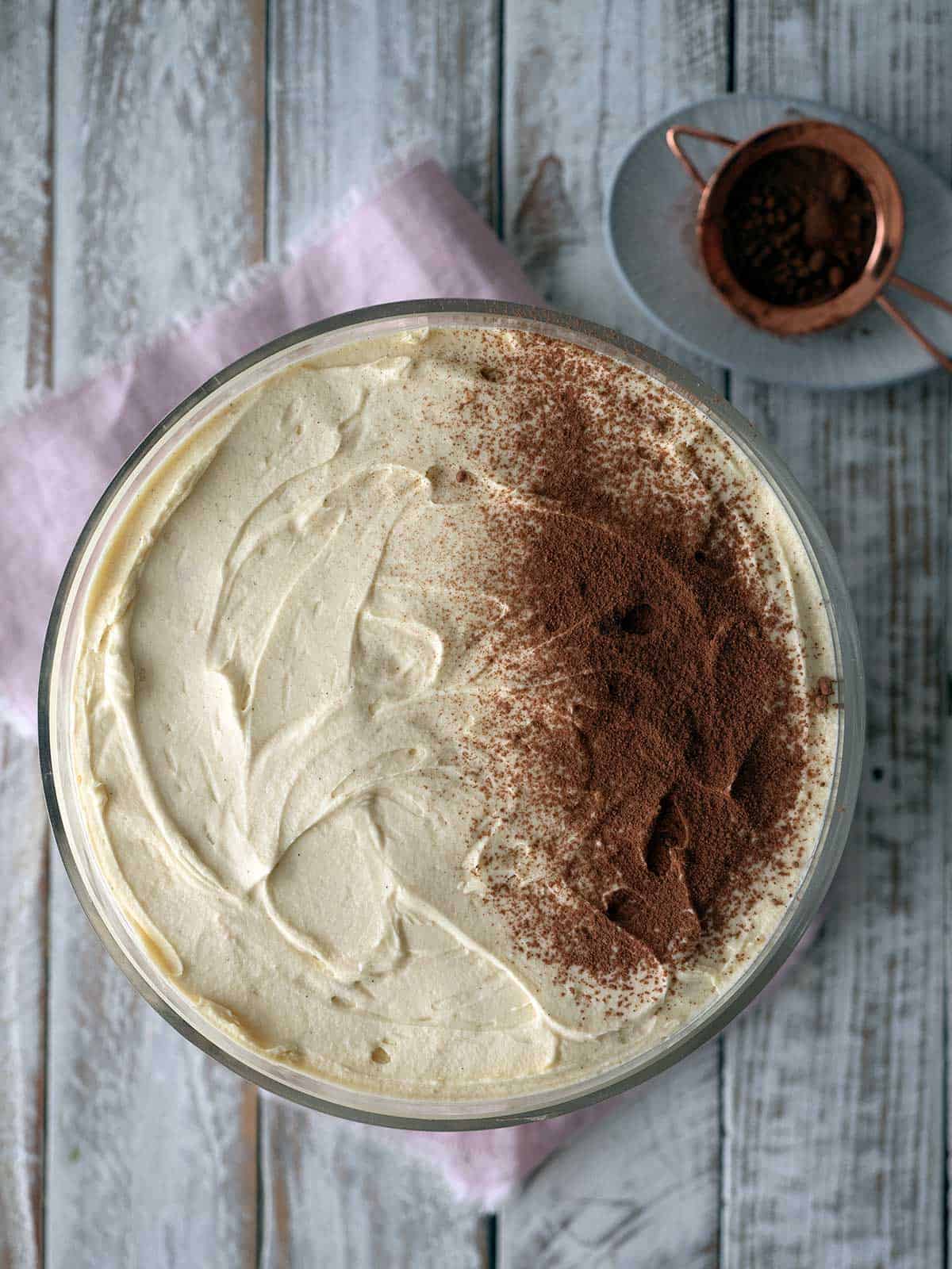 Dusting cocoa powder over the top layer of cream.