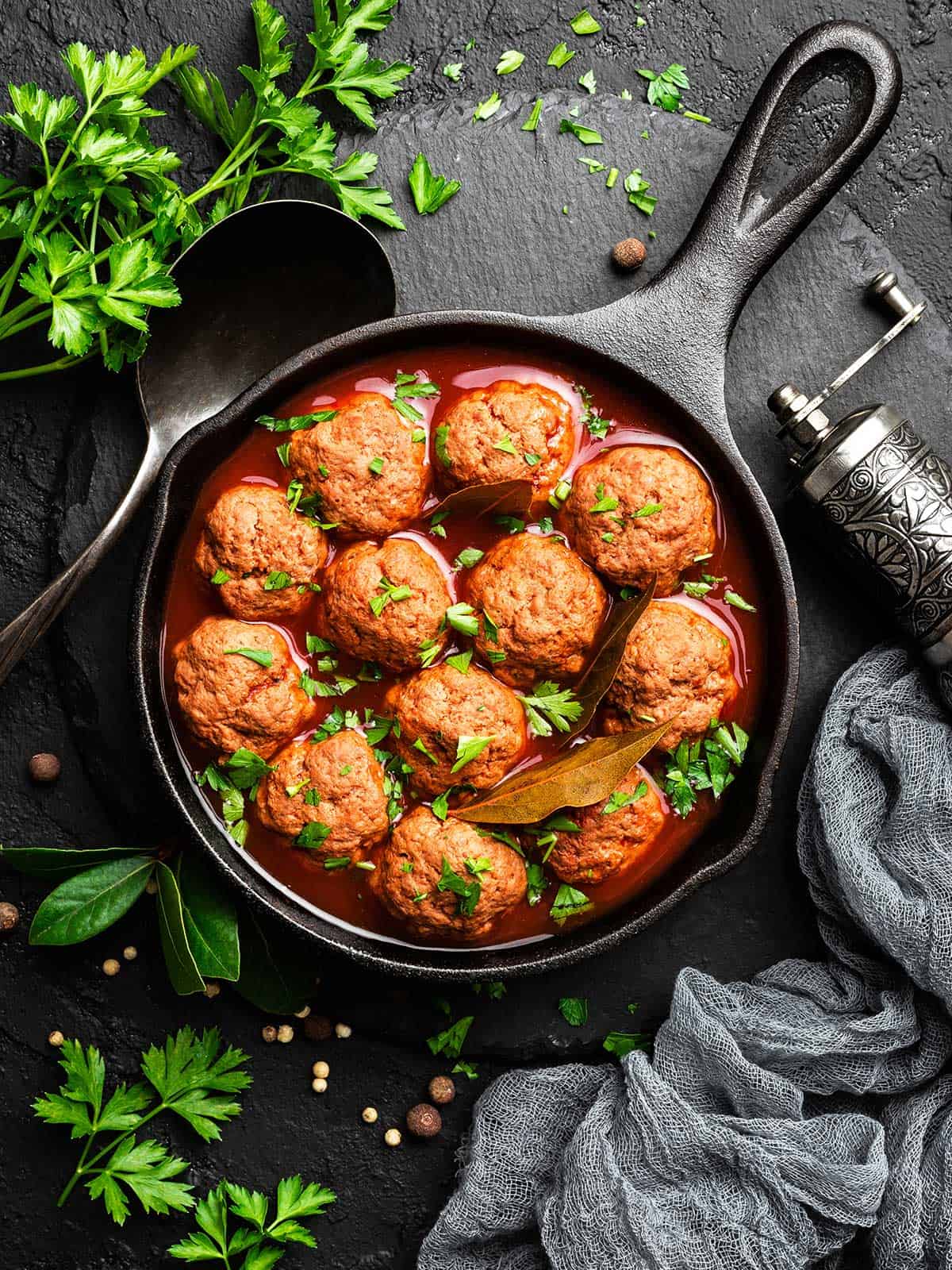 Greek meatballs in tomato sauce in a black skillet surrounded by parsley.