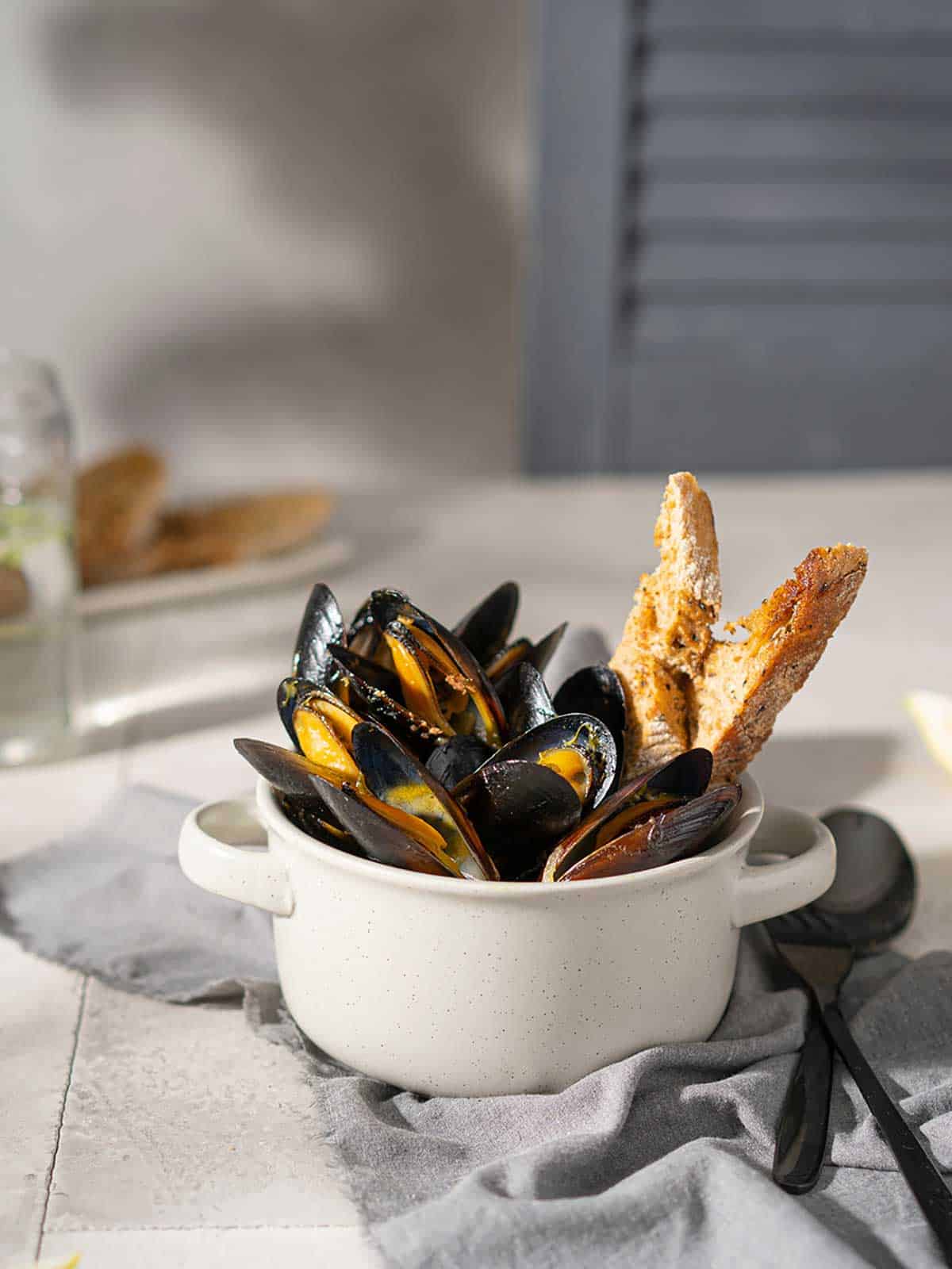 Steamed mussels and white wine saffron sauce in a white bowl with bread.