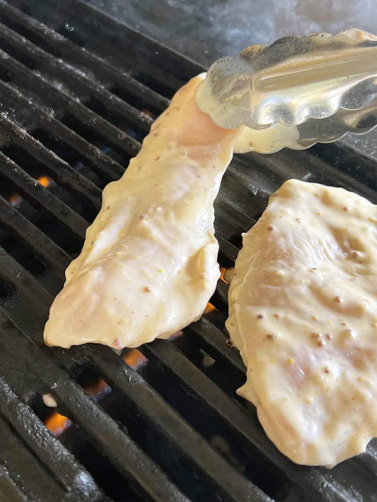 Placing mayonnaise marinated chicken on the barbecue with tongs.