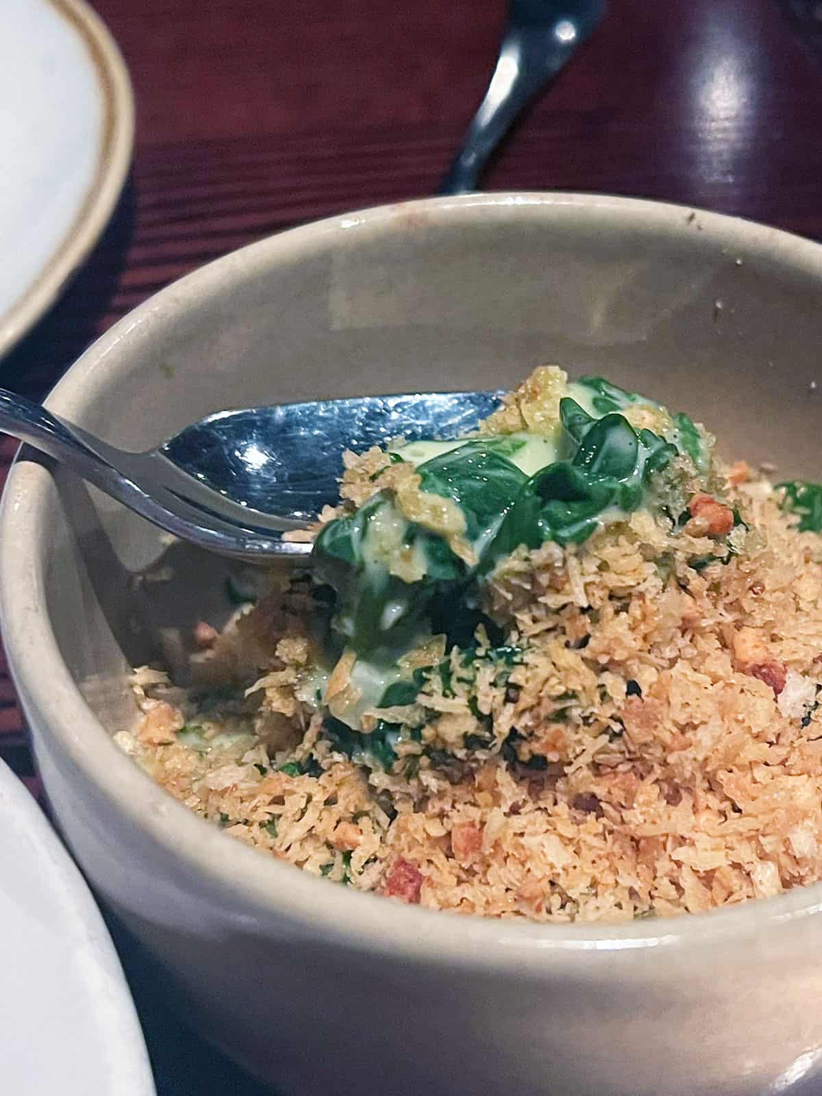 Spoon lifting out some creamed spinach from a bowl.