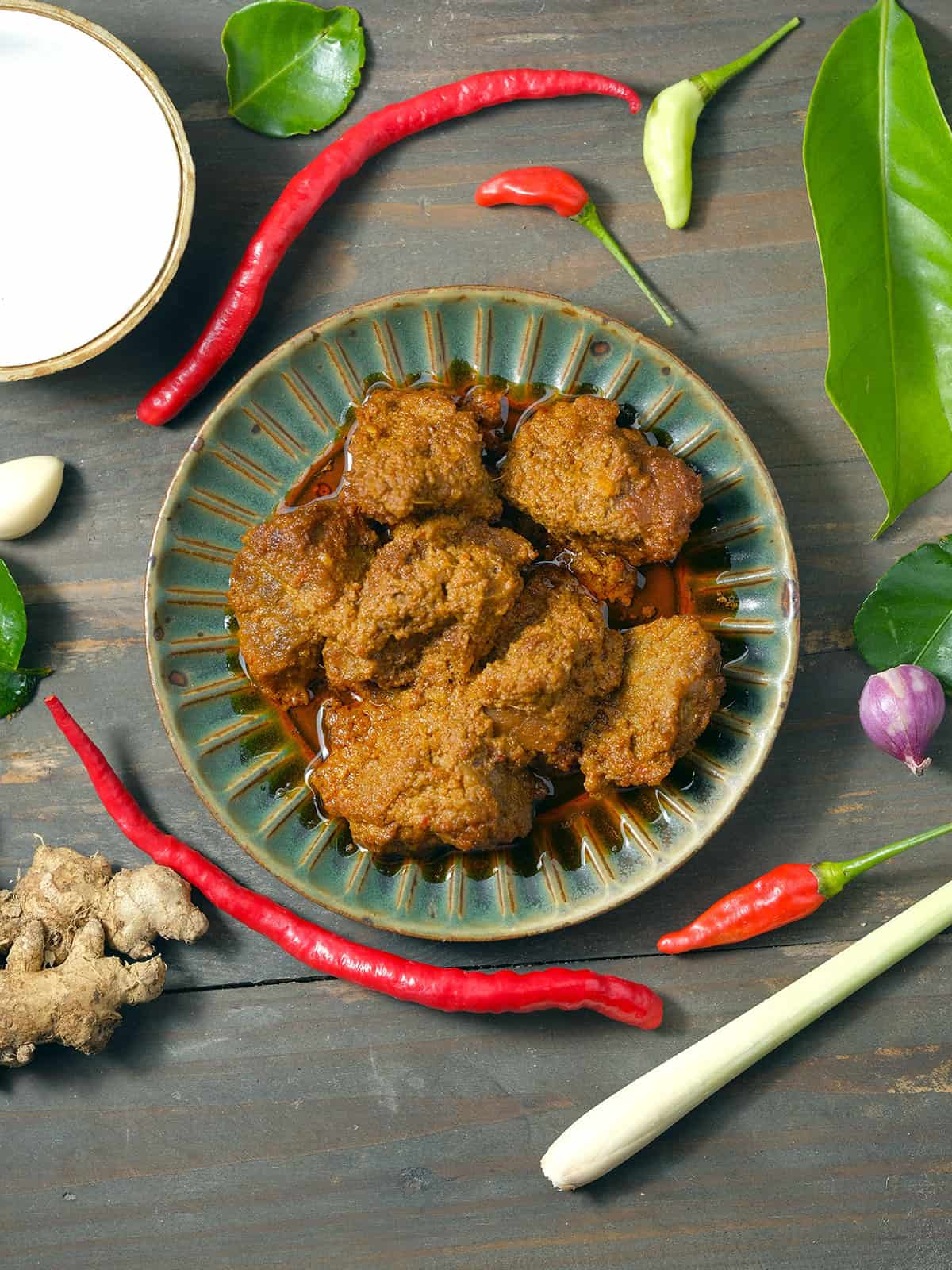 Beef rendang on a wooden board with ingredients.
