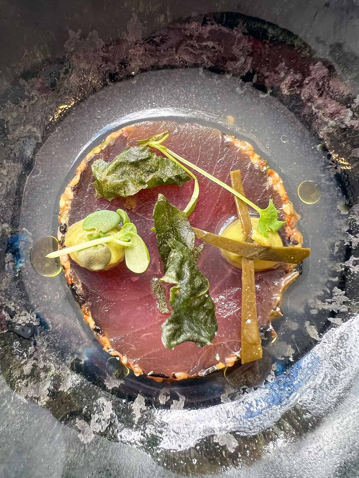 A round slice of seared tuna in a bowl with dashi.