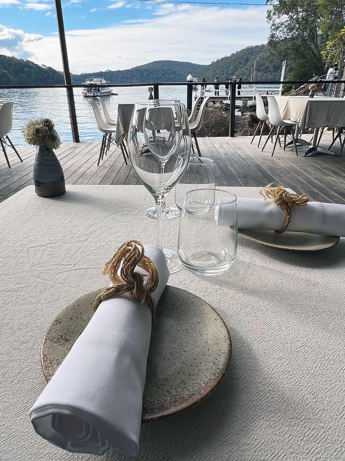 Table setting with cream table cloth, plates, and linen napkins, overlooking the river.