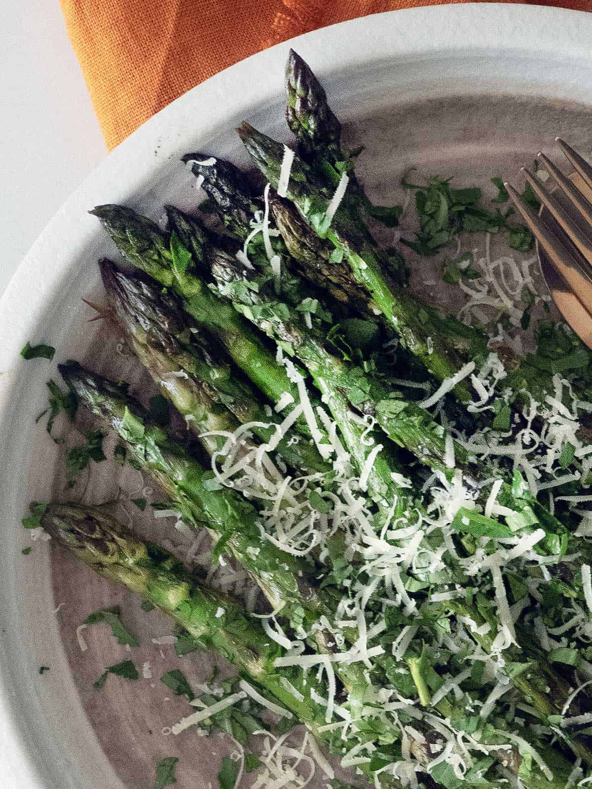 Grilled asparagus on a white plate with grated parmesan.